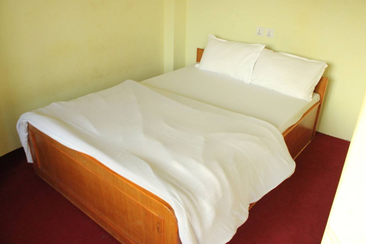 A single bed with a wooden frame and white bedding in a room with yellow walls and a red carpet.