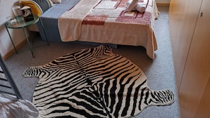 A bedroom with a bed, a zebra-patterned rug, a small table with a vase, and a window with blinds. - Gästehaus Udligenswil (Udligenswil)