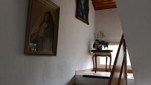 A staircase with white steps and a wooden handrail, leading to a room with a wooden ceiling and a small table with a plant. - Gästehaus Udligenswil (Udligenswil)