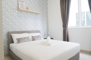 A neatly made bed with pillows and a bedside table, a wall with a leaf pattern, and a window with curtains.