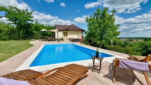 A swimming pool with lounge chairs and a table, surrounded by a house and greenery. - Luxurious home in Ludbreg (Ludbreg)