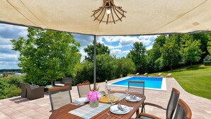 An outdoor patio with a pool, dining table, and chairs, surrounded by trees and a view of the landscape. - Luxurious home in Ludbreg (Ludbreg)