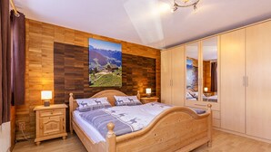 Un dormitorio con una cama de madera, una mesita de noche, un aparador, un espejo y un cuadro grande de paisaje en la pared.