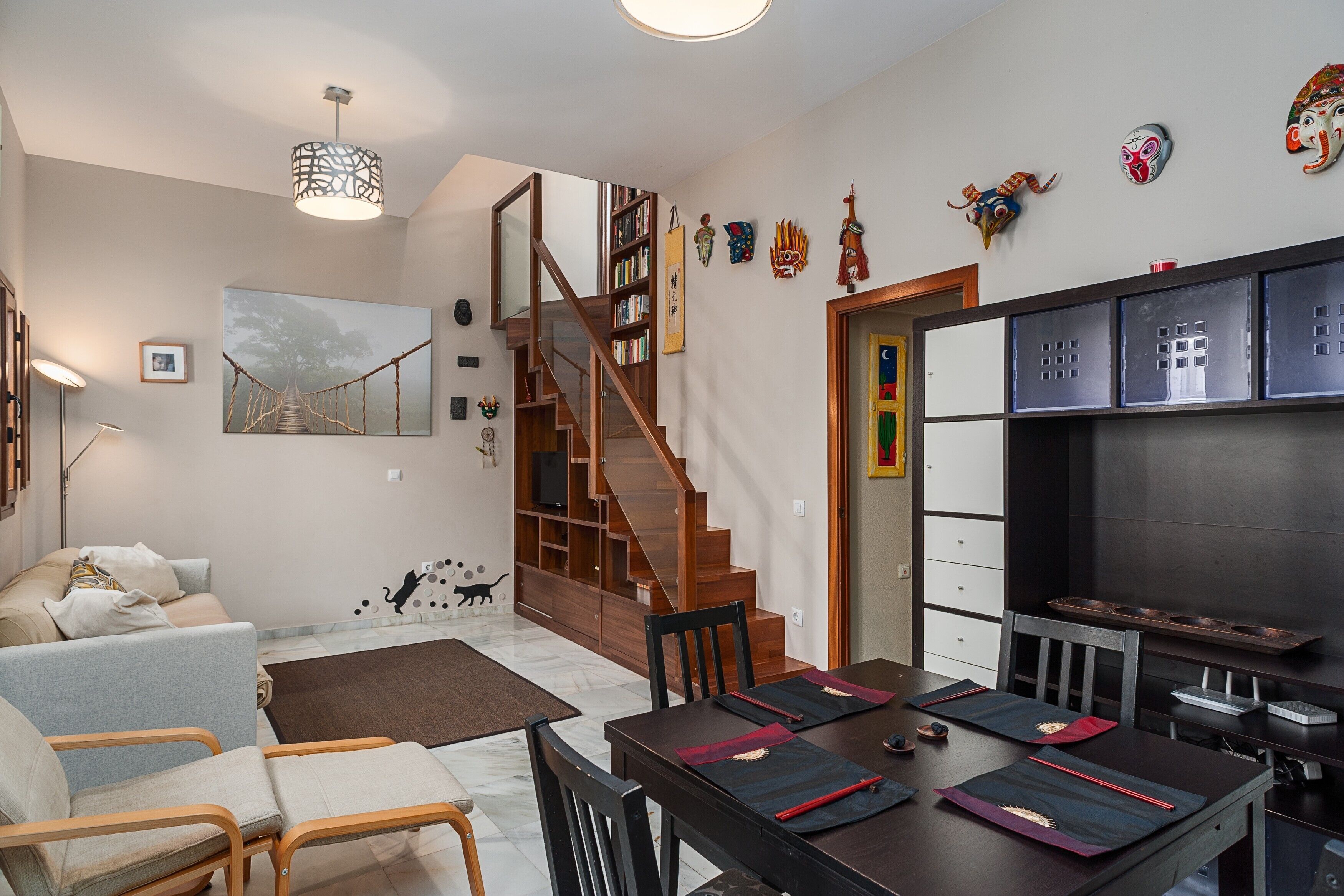 Un salon moderne avec un escalier, un coin repas agrémenté de tapis et une cuisine équipée de meubles de rangement.