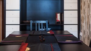 Een eettafel met zwarte placemats en rode servetten, een houten stoel en een blauwe muur met inbouwkasten.