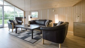A modern living room with a leather sofa, a coffee table, and a view of the outdoors through large windows.