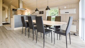 A modern kitchen with a dining area, featuring a central island, black chairs, pendant lights, and wooden flooring.