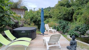 A wooden deck with outdoor seating, a hot tub, and a statue. - Le Domaine de Jade Chalet Amélie (saint andre)