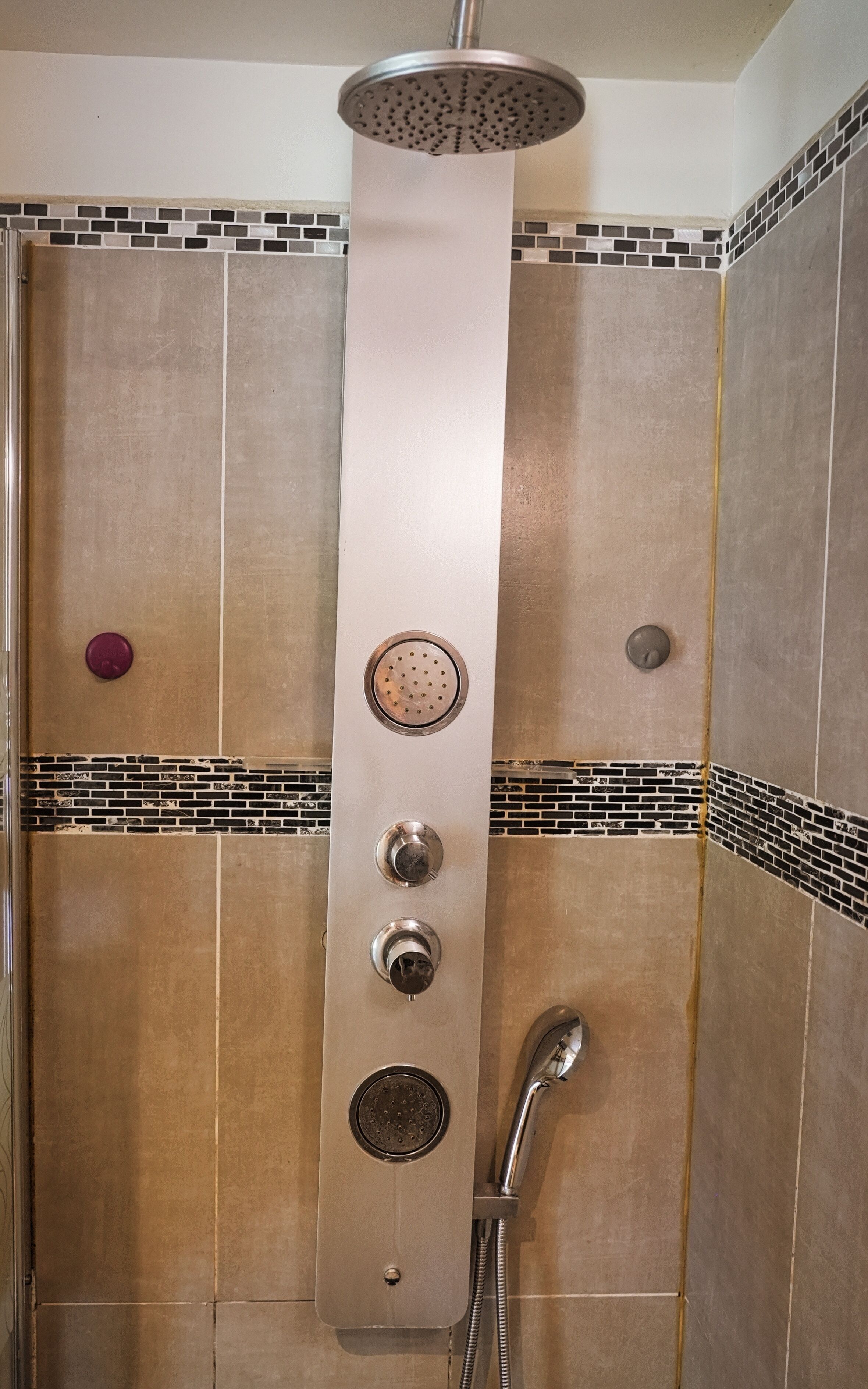 A shower with a rain showerhead, a handheld showerhead, and a handheld shower attachment.