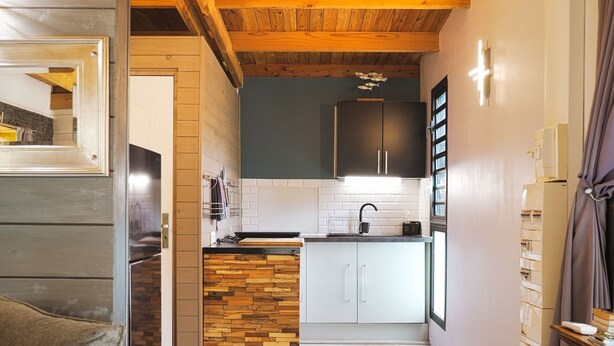 A modern kitchen with wooden beams, a herringbone-patterned island, and a view into the dining area. - Le Domaine de Jade Chalet Amélie (saint andre)