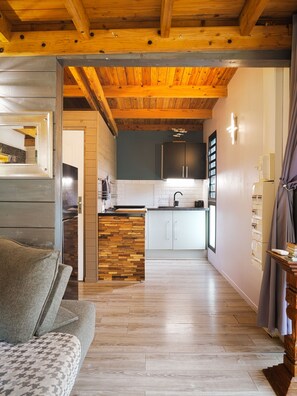 Une cuisine moderne avec des poutres en bois, un îlot central au motif en chevrons et une vue sur la salle à manger.