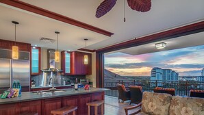Une cuisine moderne avec un coin bar, de grandes fenêtres offrant une vue sur la ville et un balcon aménagé avec des sièges.