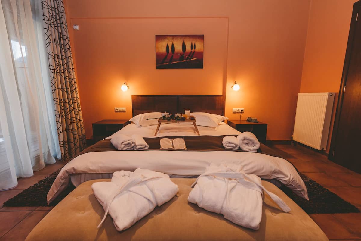 Una habitación de hotel con una cama grande, dos mesitas de noche, un cuadro en la pared y una ventana con cortinas.