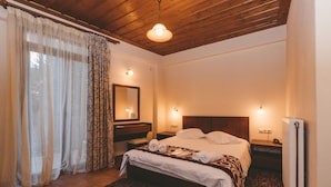A bedroom with a wooden ceiling, a bed with white linens, a bedside table, a mirror, and a radiator. - Thea Mainalou (Gortynia)