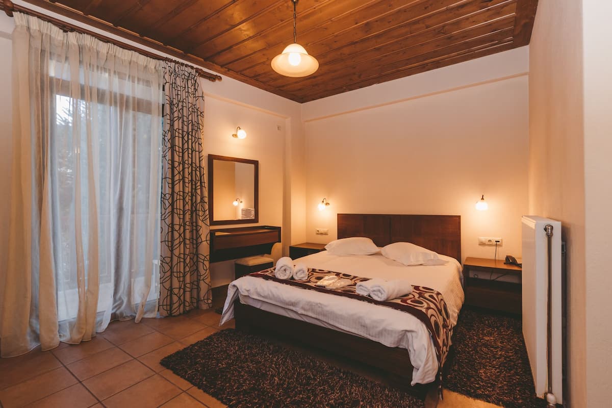 Un dormitorio con techo de madera, una cama con ropa blanca, una mesita de noche, un espejo y un radiador.
