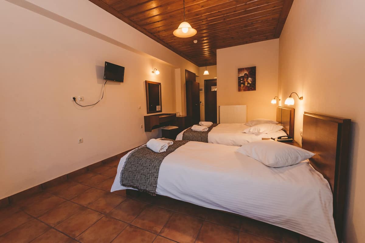 Habitación de hotel con dos camas, un televisor montado en la pared y techo de madera.