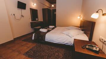 Un dormitorio con cama, mesita de noche, lámpara y televisor montado en la pared.