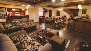A spacious living room with a high ceiling, wooden beams, and a cozy fireplace. There is a dining area with a bar and a staircase leading to an upper level. - Thea Mainalou (Gortynia)