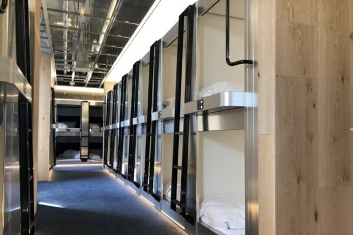 A corridor with bunk beds, a wooden wall on one side, and a metal ceiling with exposed pipes.