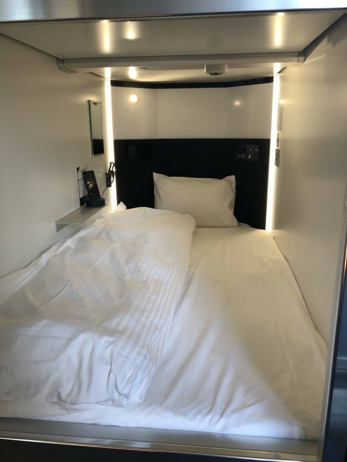 Una cama con sábanas blancas, cabecera e iluminación colgante.