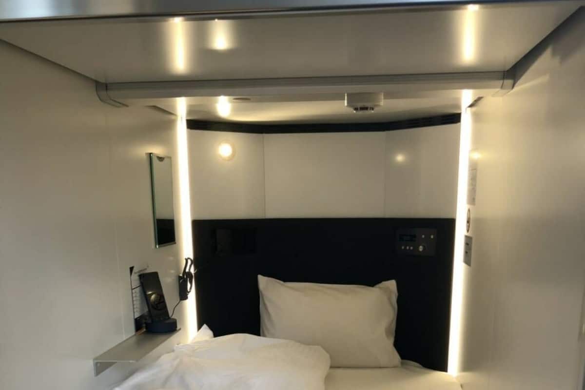 Una cama con sábanas blancas, un cabecero y una mesita de noche con un teléfono y una lámpara.