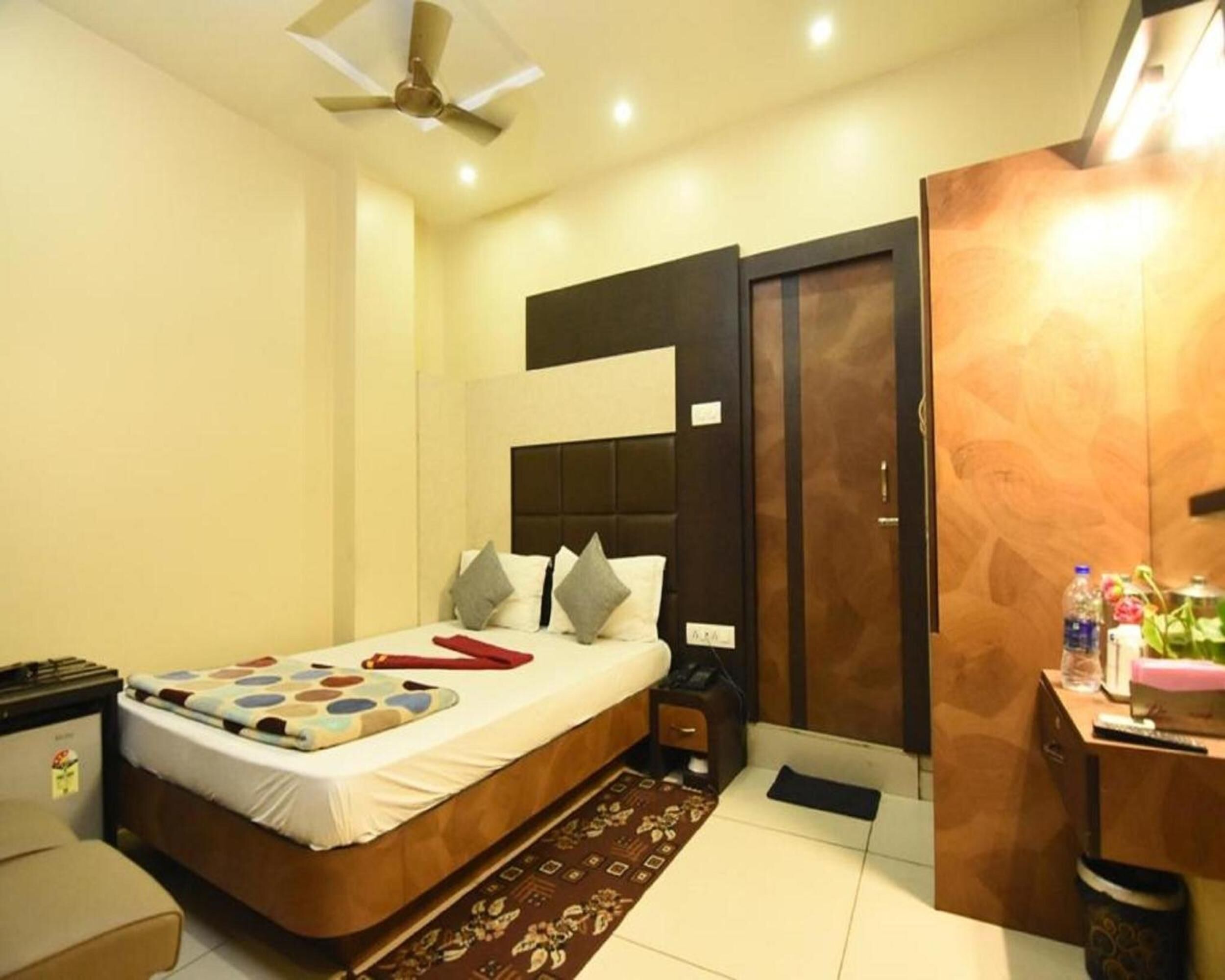 A hotel room with a bed, bedside table, nightstand, wardrobe, and a desk with a chair.