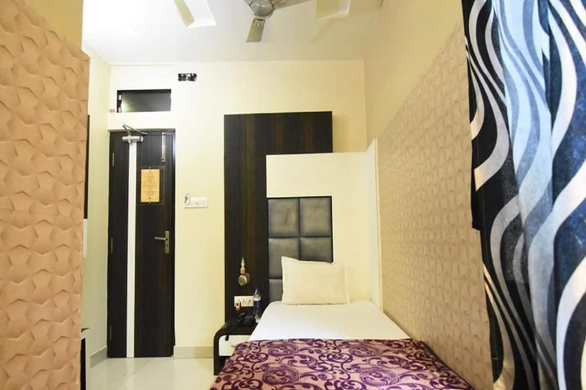 A bedroom with a bed, a nightstand, a wall-mounted TV, a ceiling fan, and a door with a sign.