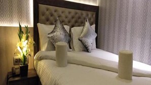 A neatly made bed with two pillows and two cylindrical bedside tables, one with a plant. - Nu Blue Moon Guest House (Howrah)