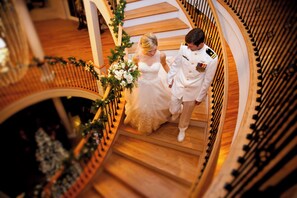 Un couple de jeunes mariés descendant un escalier en bois, une guirlande de fleurs à la main.