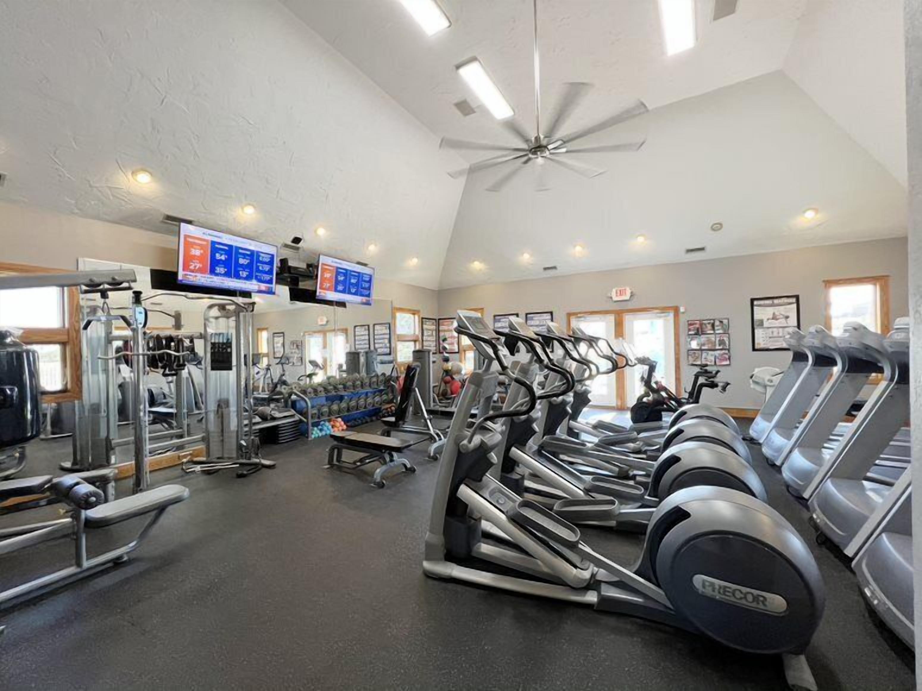 Ein Fitnessstudio mit Laufbändern, Kraftgeräten und einem Deckenventilator.