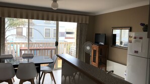 Un balcón con un cartel de precaución, un televisor en un mueble y un refrigerador.