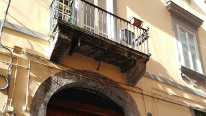 Una puerta de madera grande con entrada en arco, un balcón con barandilla de metal y un edificio con fachada amarilla.