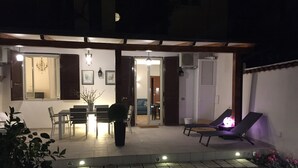 Un patio cubierto con comedor, una silla de descanso y un pequeño jardín.