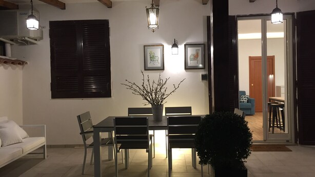 Un comedor con una mesa, sillas y una planta en maceta. Hay luces en el techo, un aire acondicionado de pared y una puerta que conduce a otra habitación.