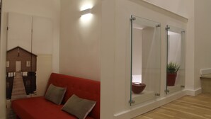 Una habitación moderna con un sofá rojo, una partición de vidrio y una pequeña planta en maceta.