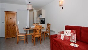 Un espace de vie compact comprenant un coin repas, un canapé rouge et une petite cuisine.