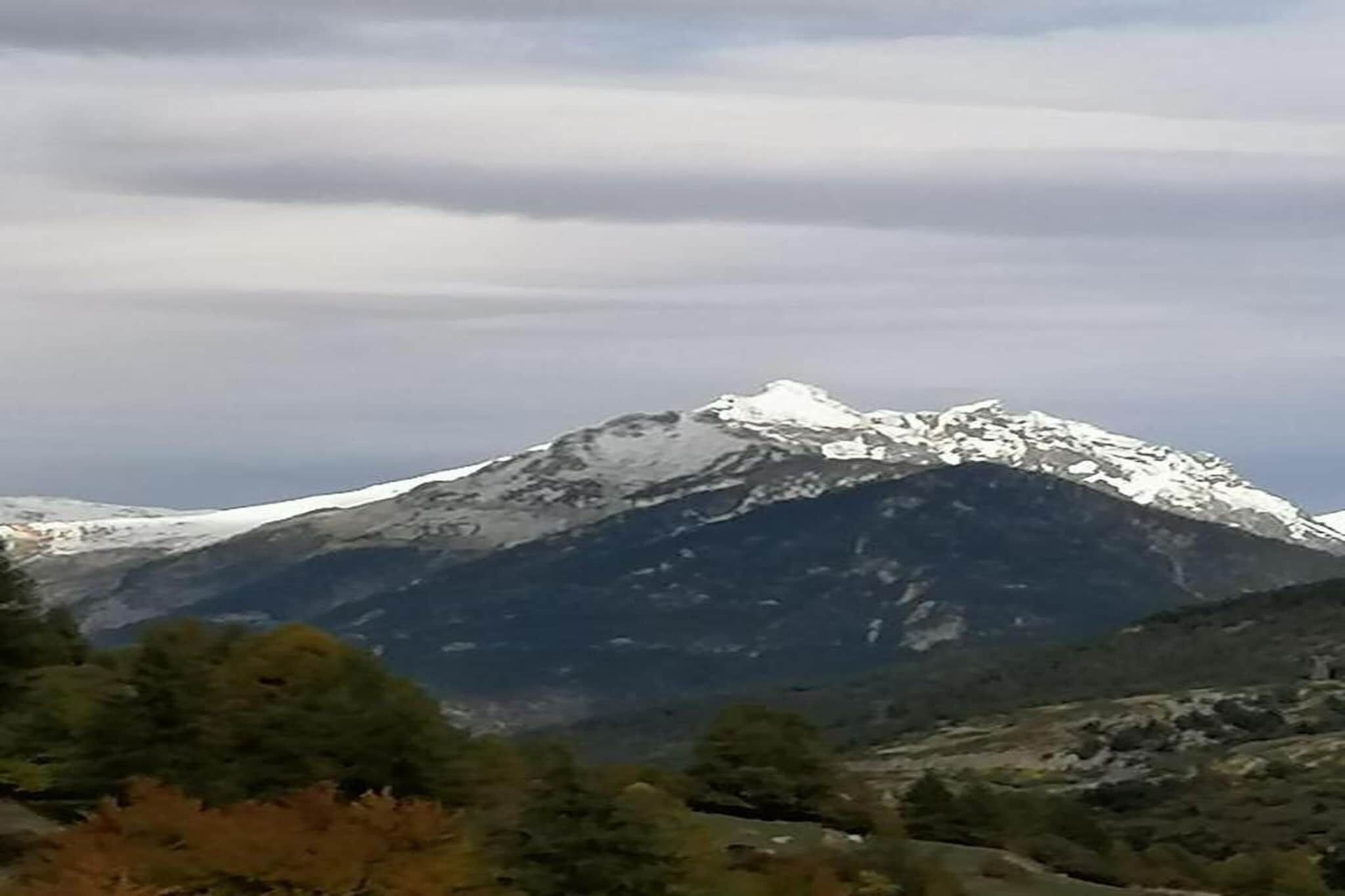 Een berg met besneeuwde toppen en een vallei met schaarse begroeiing.
