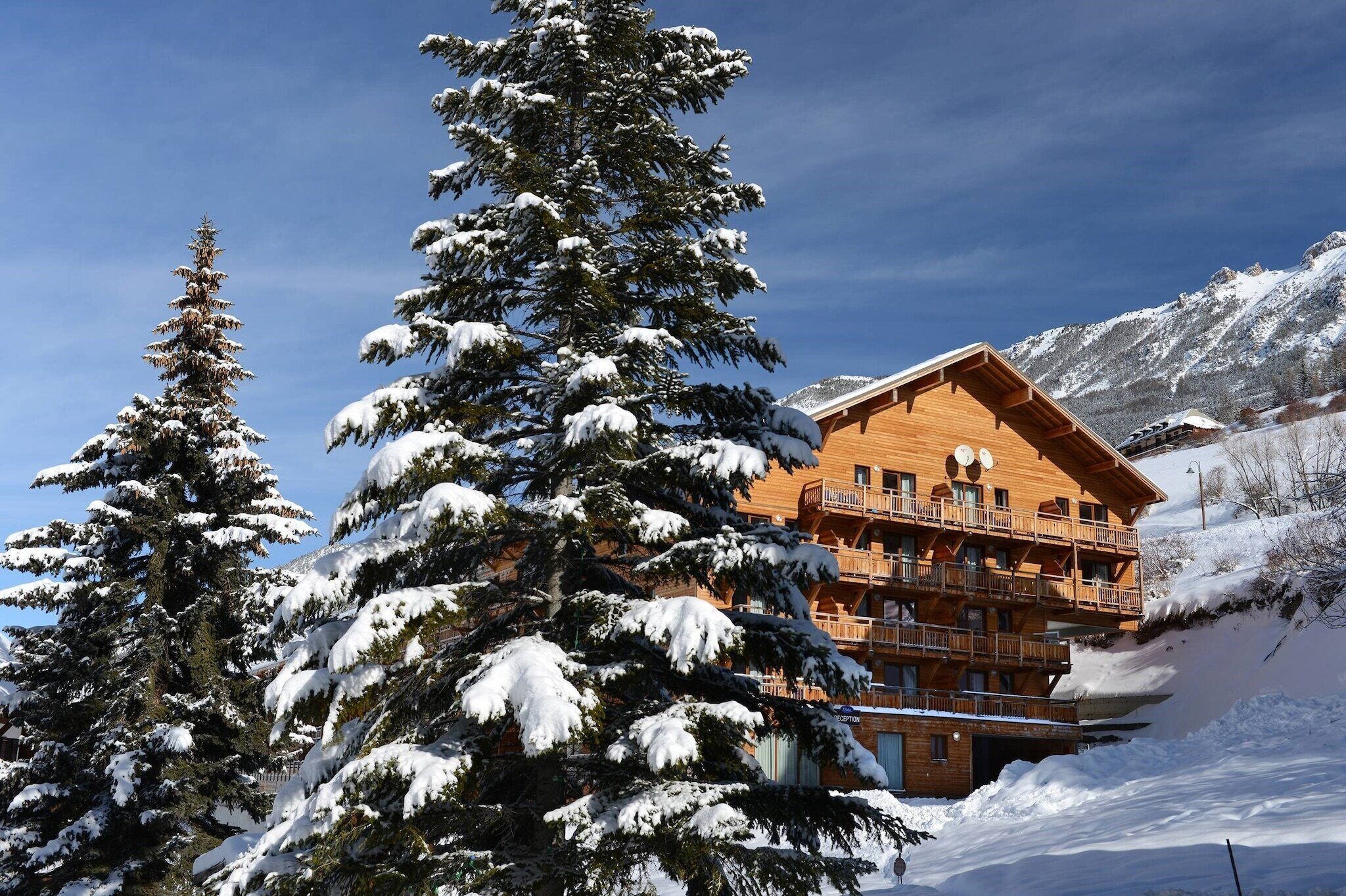 Un chalet en bois doté de plusieurs balcons, entouré d’arbres et de montagnes couverts de neige.
