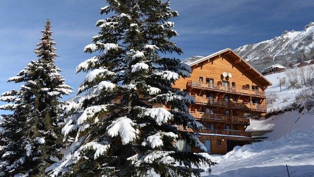Un chalet en bois doté de plusieurs balcons, entouré d’arbres et de montagnes couverts de neige.