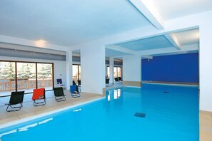 Ein hallenbad mit klarem, blauen Wasser, umgeben von weißen Wänden und großen Fenstern.
