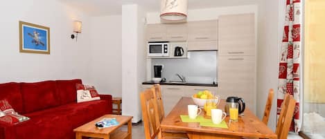 A compact living space with a red sofa, wooden dining table, and a kitchenette.
