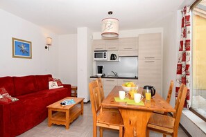A compact living space with a red sofa, wooden dining table, and a kitchenette. - Slopeside Chalet in Vars (VARS)