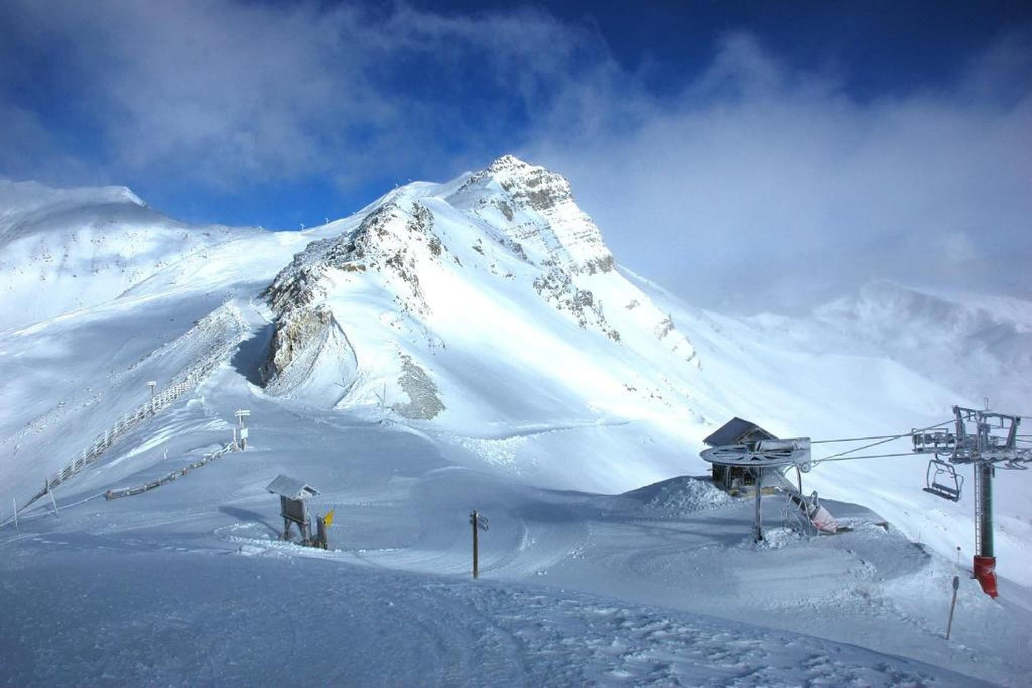 Une montagne enneigée, avec un télésiège et un petit bâtiment.