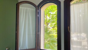 Quarto com três janelas, cada uma com cortina. As janelas têm moldura de madeira escura e as paredes são verdes.