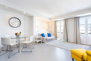 A modern living room with a glass dining table, white chairs, a sofa with blue cushions, and a yellow armchair. - Rooms & Suites Loft 2H - Arrecife, Lanzarote (Arrecife)