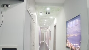 A long, narrow hallway with a polished floor, white walls, and a ceiling with recessed lighting. There is a poster on the right wall and a door at the end of the hallway. - B&B Nazionale (Naples)