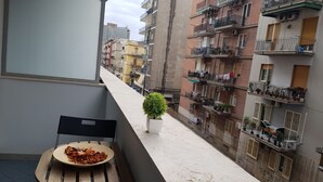 A balcony with a table, a potted plant, and a view of a residential area with multi-story buildings. - B&B Nazionale (Naples)