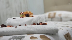 Two neatly folded white towels with dried flowers and a small green flower on a bed with a white and brown patterned bedspread. - B&B Nazionale (Naples)