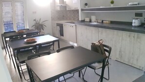 A modern kitchen with a dining area, featuring a long table, chairs, and a countertop with appliances. - B&B Nazionale (Naples)