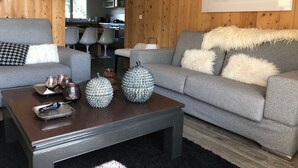 Una sala de estar moderna con un sofá gris, una mesita de centro con objetos decorativos y una pared de madera con una obra de arte de un ciervo.